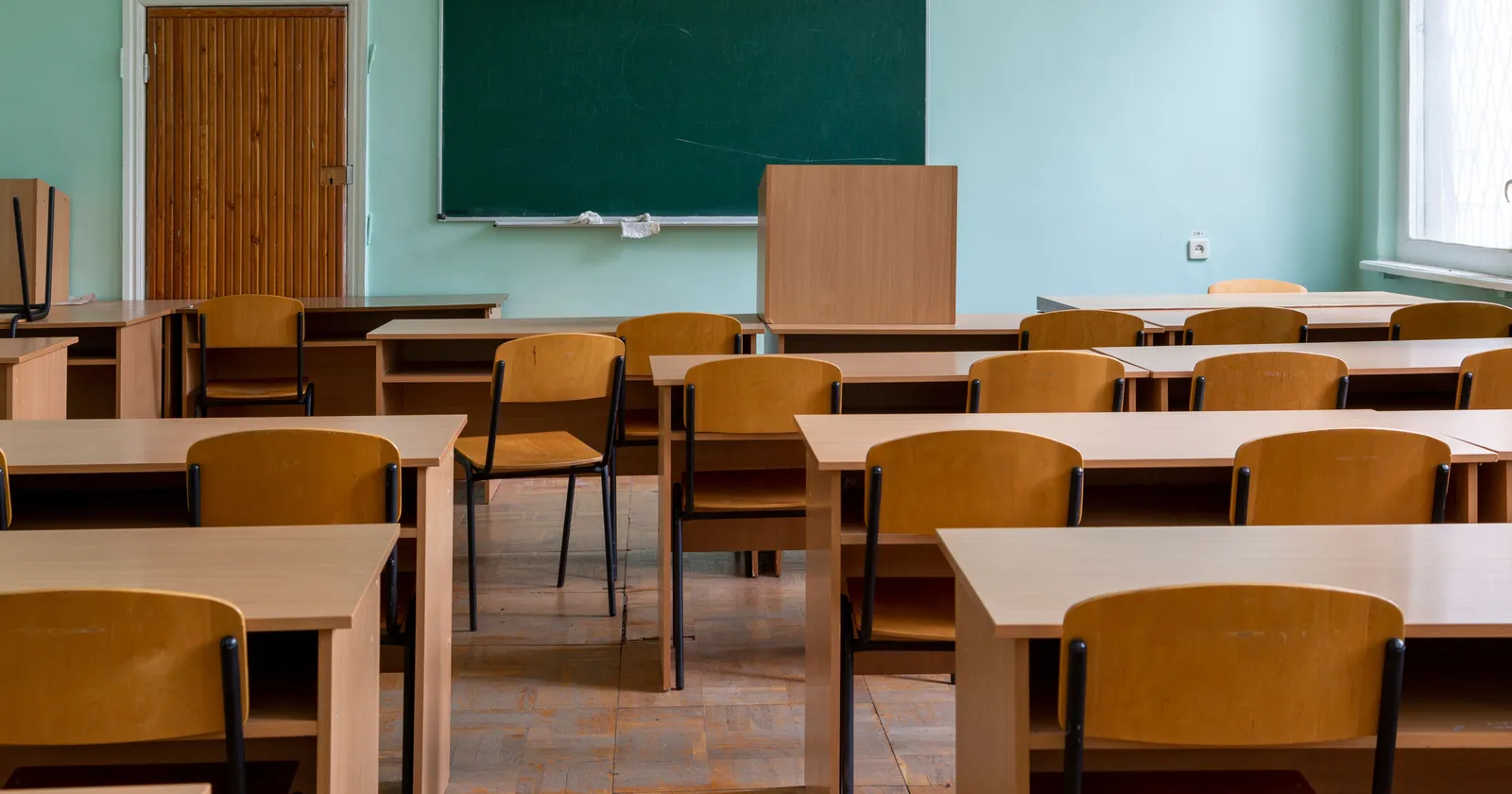 An empty ordinary classroom with wooden desks and chairs and a green chalkboard, with no lab benches